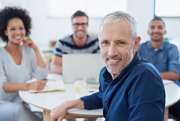 taking-his-team-new-places-portrait-group-designers-work-office man at office table with co-workers back to work with SSDI